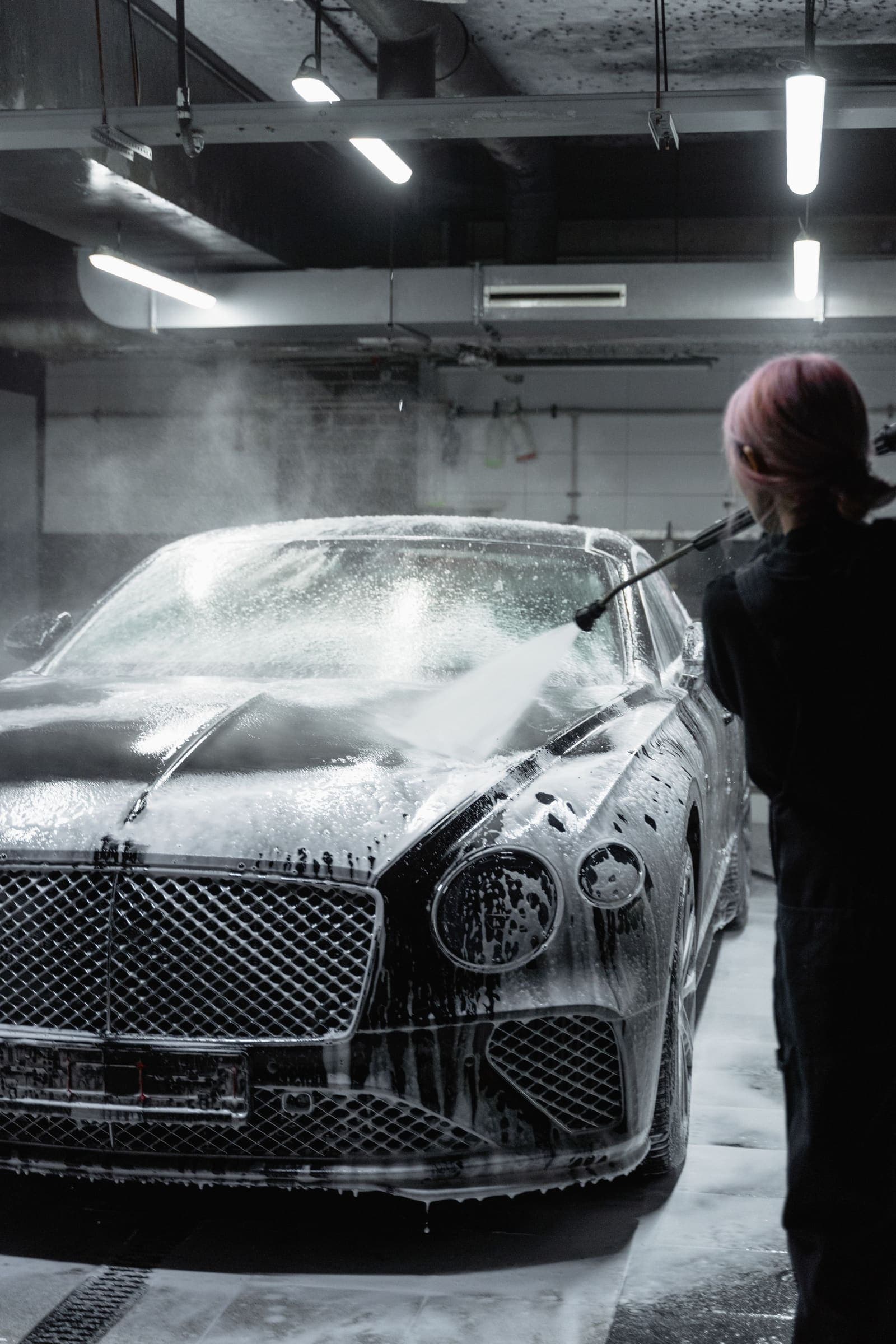 Car covered in snow foam being pressure washed