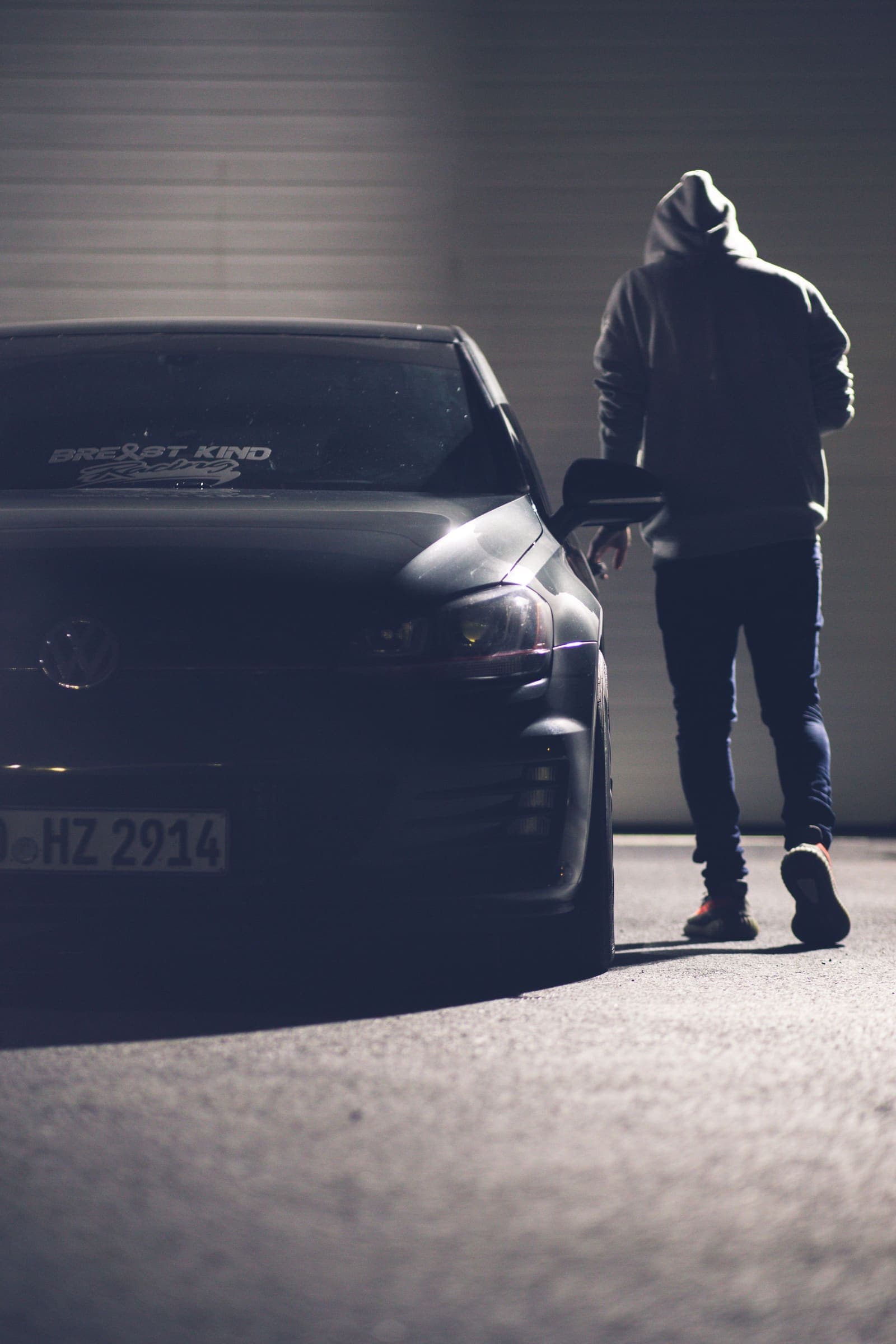 Hooded figure walking towards a parked car at night
