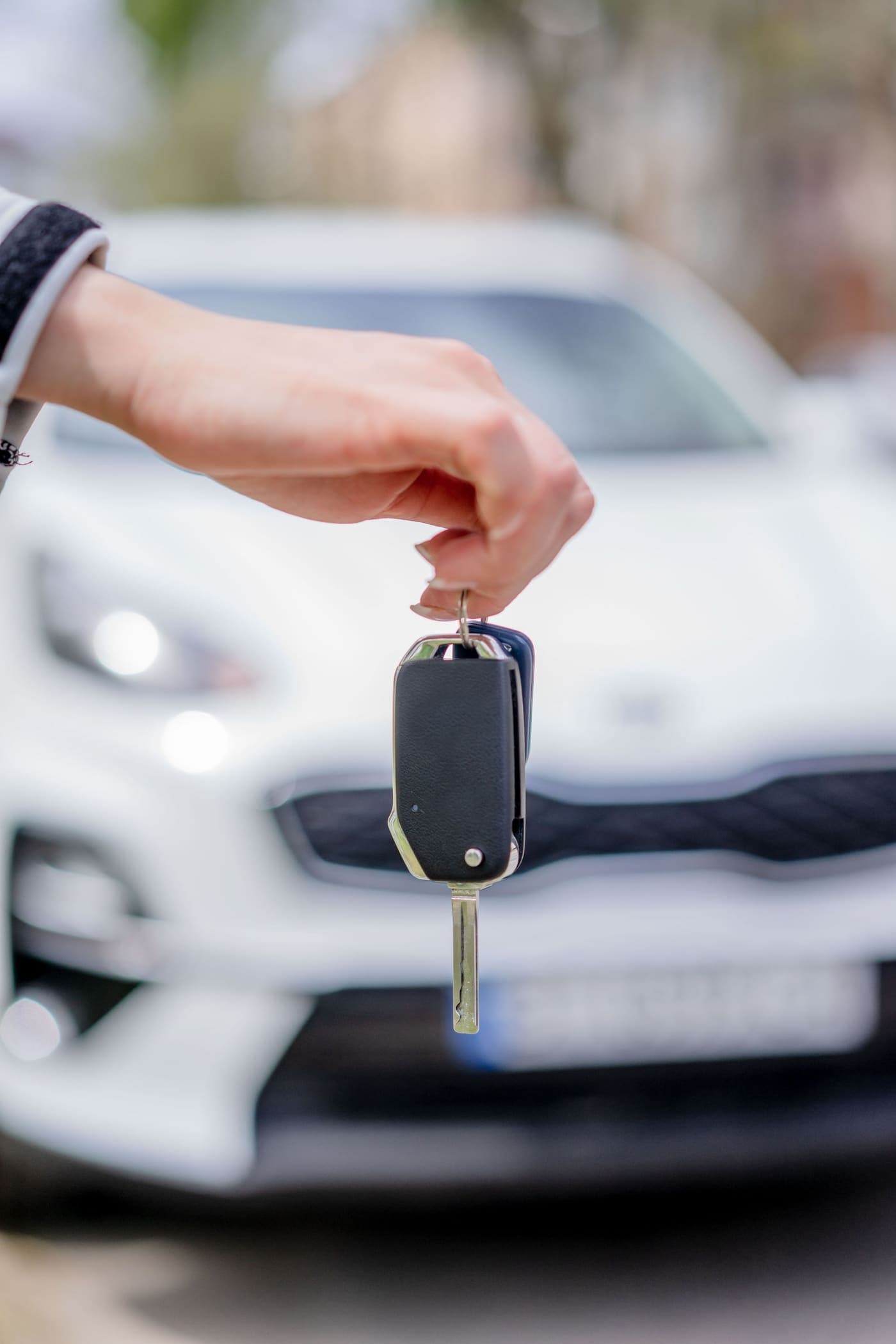 Car key held up in front of a white car
